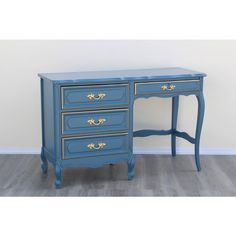 a blue desk with two drawers and gold trimmings on the top, against a white wall