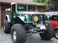 a large green truck parked in front of a red car next to a brick building