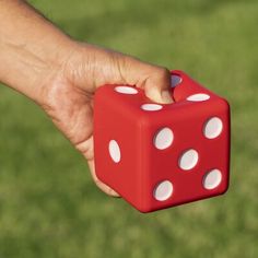 a hand holding a red and white dice in it's right hand on the grass