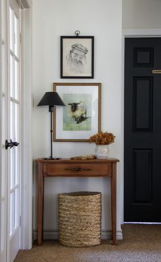 an entryway with a table, lamp and pictures on the wall next to it