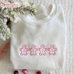 a white shirt with pink letters on it next to some ornaments and a christmas tree