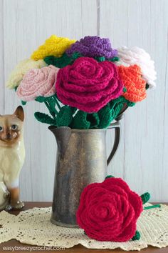 crocheted flowers in a vase on a doily next to a cat figurine