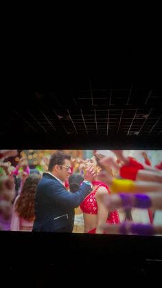 a man standing in front of a large screen on top of a wall next to dancers