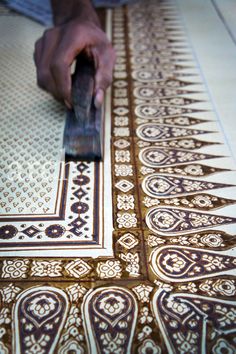 a person is using a knife to cut out an intricately designed tile pattern on the floor