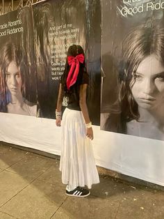 a woman standing in front of a wall with posters on it and wearing a red scarf around her neck