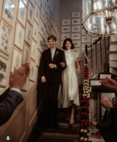 a man and woman are walking down the stairs in front of wall with pictures on it