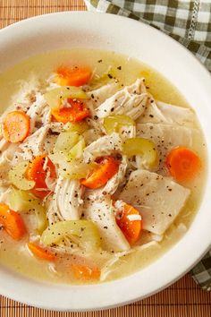 a white bowl filled with chicken and carrots on top of a wooden tablecloth