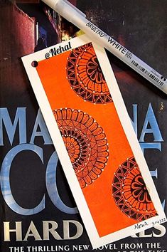 an orange and black bookmark sitting on top of a magazine with a pencil next to it