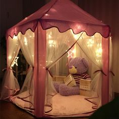 a teddy bear sitting in a pink tent with lights on the ceiling and curtains around it