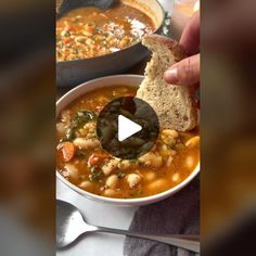 a person holding a piece of bread over a bowl of soup