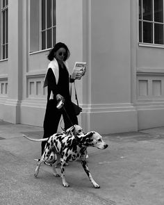 a woman walking a dalmatian dog on a leash while reading a book in front of a building