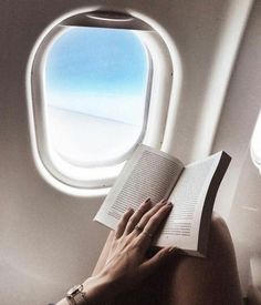 a woman reading a book while sitting on an airplane with the window looking out at the ocean