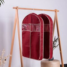 two red storage bags hanging on a wooden rack next to a potted plant and vase