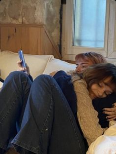 two women sitting on a couch with their arms around each other and one holding a cell phone