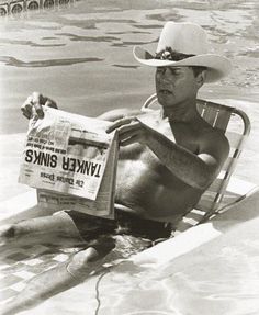 an old photo of a man sitting in the water with a newspaper on his lap