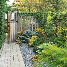 a small garden with lots of plants and rocks in it's path leading to an open wooden gate