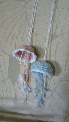 two little jellyfish necklaces hanging from a string on a bed with white and blue wallpaper