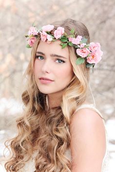 a woman with long blonde hair wearing a wreath of pink flowers on her head and in the snow