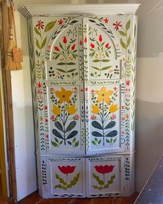 an ornate painted armoire with flowers and leaves on the doors is in front of a doorway