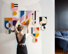 a woman standing in front of a wall with art on it and another photo of a bed behind her