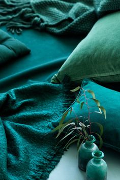 two green vases sitting on top of a bed next to pillows and blankets with plants growing out of them