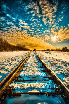 a train track with the sun setting in the background and snow on the ground below