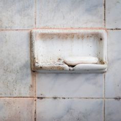 an old dirty toilet in the middle of a tiled wall