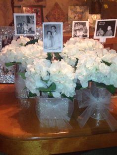 white flowers in clear vases on table with pictures and glittered frames behind them