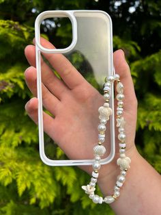 a person holding up a phone case with shells and pearls attached to the back of it