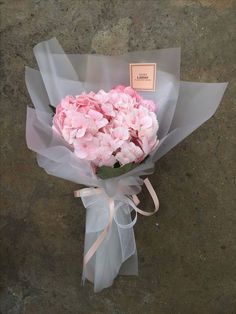 a bouquet of pink flowers is wrapped in gray paper and tied with a white ribbon