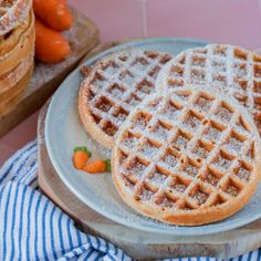 two waffles sitting on top of a plate covered in powdered sugar next to carrots