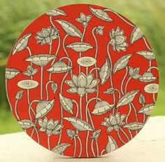 a red plate with white flowers on it sitting on a table next to some grass