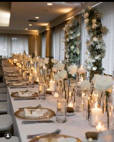 a long table is set with candles and flowers in glass vases, plates and silverware