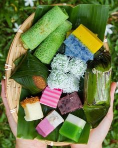 a person holding a basket filled with different types of food on top of green leaves