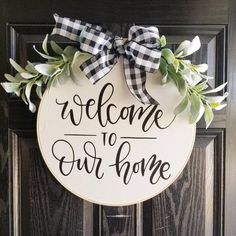 a welcome sign hanging on the front door with greenery around it that says, welcome to our home