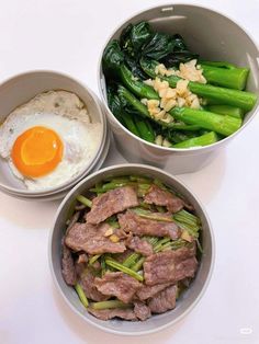 three bowls filled with meat and vegetables next to an egg on top of a white table