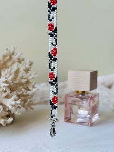 a beaded bracelet next to a bottle of perfume on a white surface with corals in the background