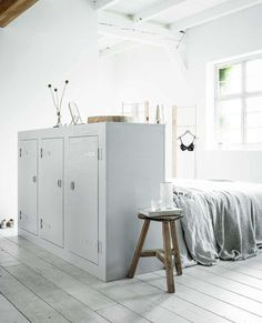 a white room with a bed and two lockers on the wall next to a stool