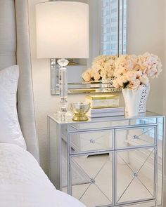 a mirrored nightstand with flowers and a lamp on top