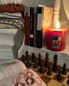 a candle and some books on a shelf next to a chess board with candles in it