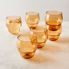 five yellow glass cups sitting on top of a white counter next to an orange bowl