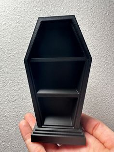 a hand holding an empty black shelf in front of a white wall