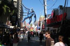 people are walking down the street in front of some shops and buildings with a giant blue man on it