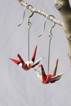 two red and white bird shaped earrings hanging from hooks on a tree branch with water in the background