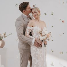 a bride and groom standing next to each other in front of a wall with flowers