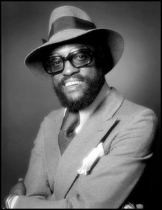 a man in a suit and hat poses for a black and white photo with his arms crossed