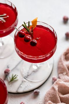 two glasses filled with red liquid and garnished with cranberries on the side