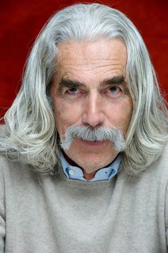 an older man with long grey hair and a moustache looks at the camera