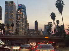 several cars driving on a freeway in front of tall buildings and palm trees at dusk