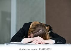 a woman is sitting at a desk with her head on her hands and looking down